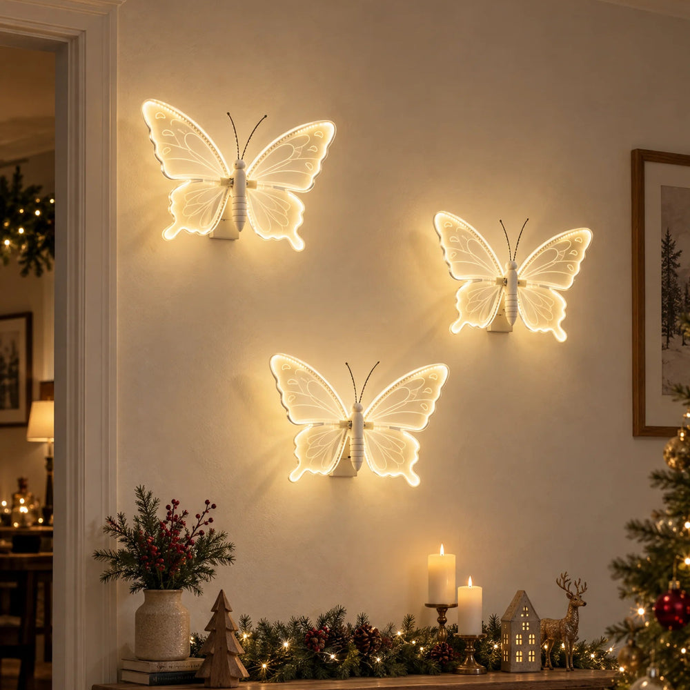 Three glowing butterfly wall lights mounted on a wall in a cozy holiday living room, with a wooden console table, candles, greenery, and a decorated Christmas tree nearby.